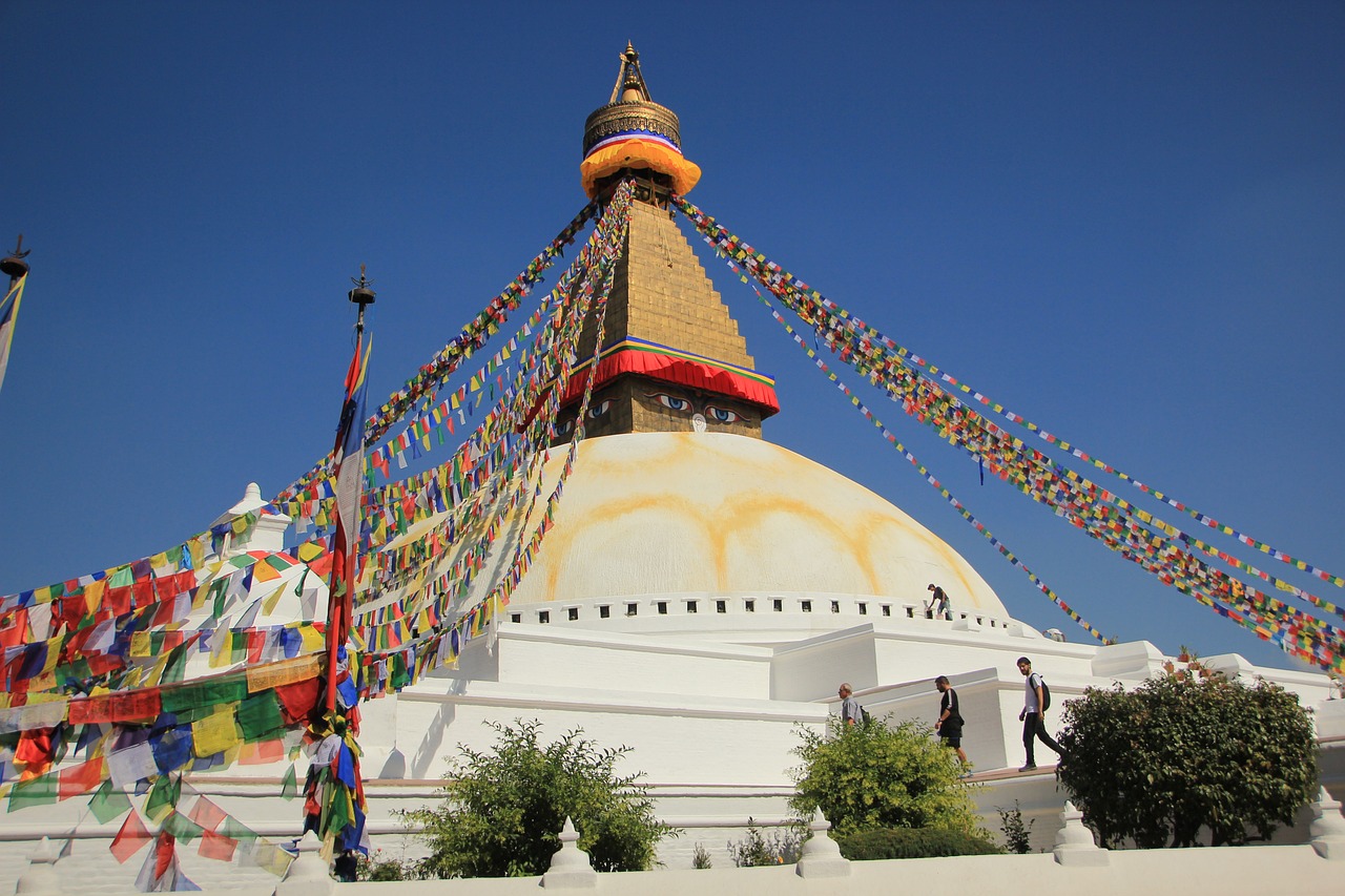 Boudhanath Stupa in Kathmandu with white dome, colorful prayer flags, and golden spire featuring all-seeing eyes under a clear blue sky.