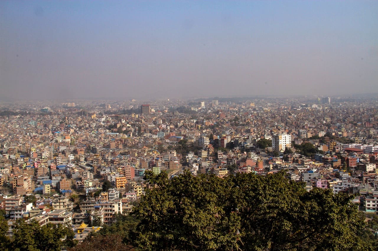 Bustling Kathmandu cityscape with historic temples, busy streets, and the Himalayas in the background under a clear sky.