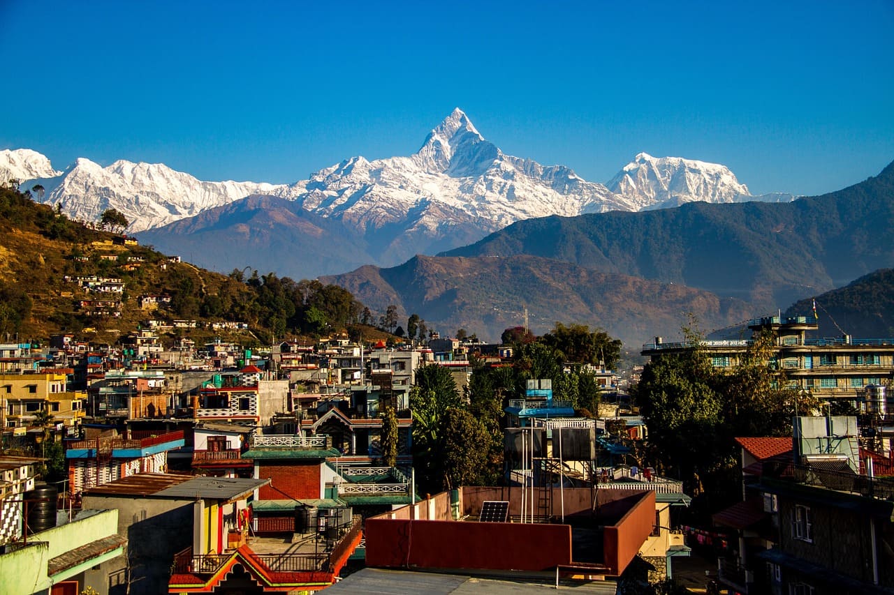 Scenic Pokhara Valley with Phewa Lake, green hills, and Annapurna mountains under a clear blue sky.