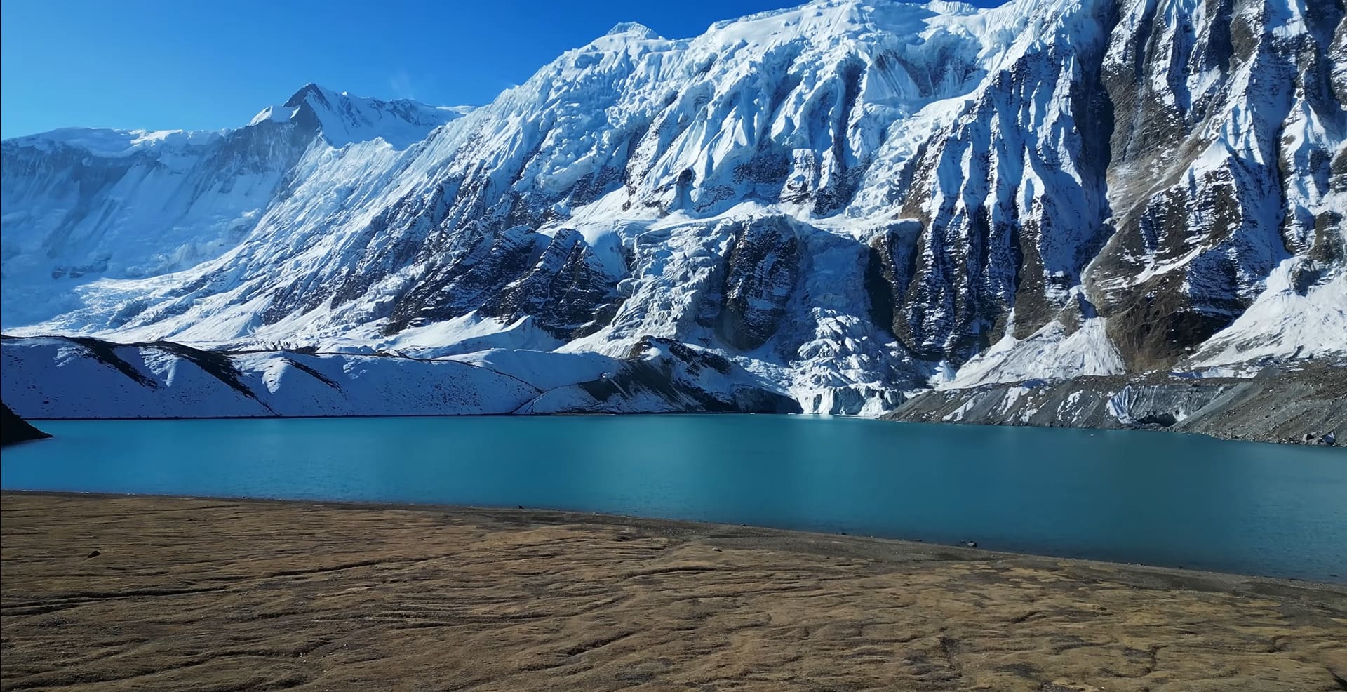 Scenic view of Tilicho Lake surrounded by towering snow-capped mountains