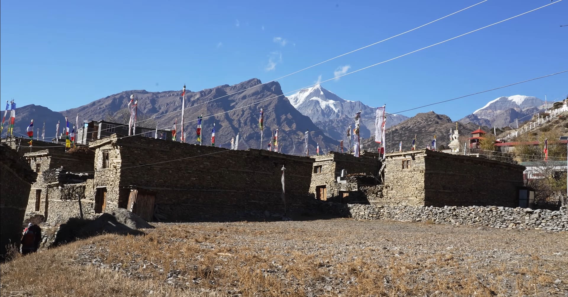 Stone house with wooden windows along the Annapurna Circuit trail, surrounded by mountains and greenery.