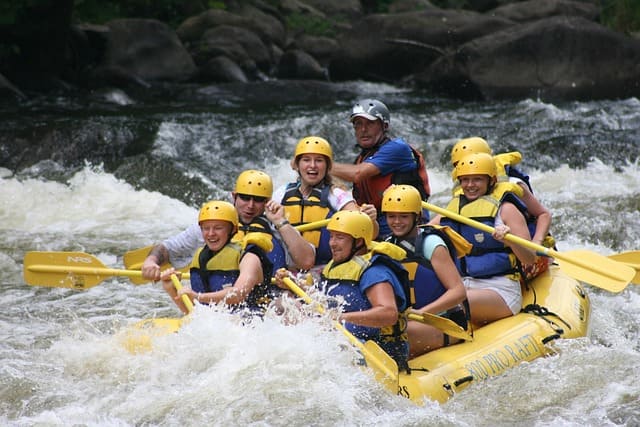 Travelers wearing life jackets and helmets, excitedly rafting through the rapids of the Trishuli River amidst scenic greenery.